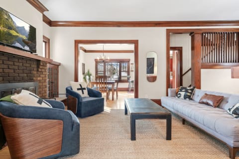 Cozy living room showcasing a brick fireplace, mounted TV, blue armchairs, and a wooden coffee table.