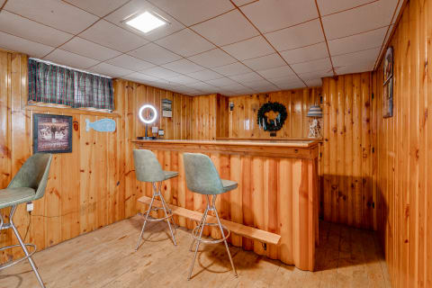 Interior view of a wooden home bar area with bar stools and decorative elements.