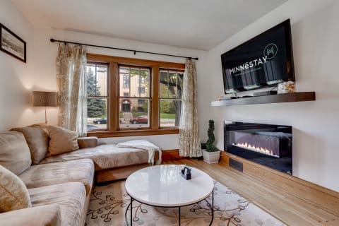 A cozy living room featuring a sectional couch, large windows, and an electric fireplace.