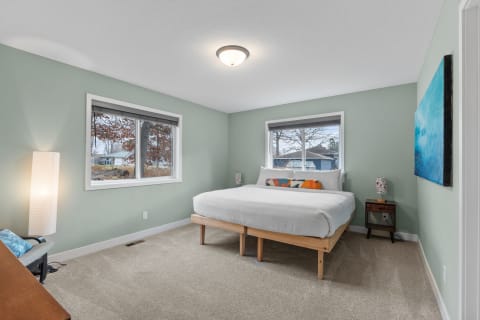 A bedroom with green walls, a bed, and two windows providing natural light.