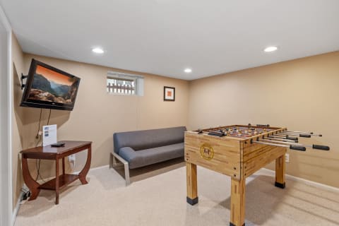 A basement room with a foosball table, gray sofa, and wall-mounted TV.