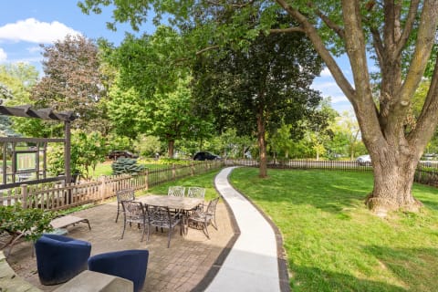 Outdoor backyard with a stone patio, table, and lush trees under a blue sky.