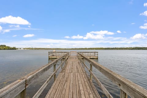 A wooden pier leading into a calm lake with a person fishing at the end.