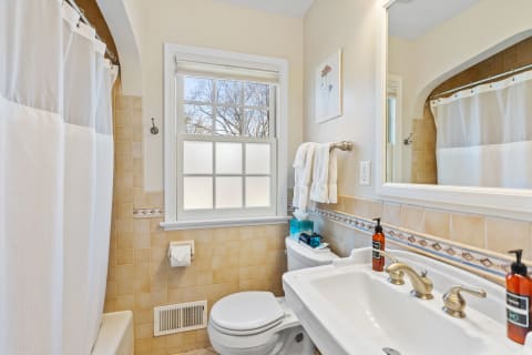 Neatly designed bathroom with a white shower curtain, beige tiled walls, and a bright sink area.