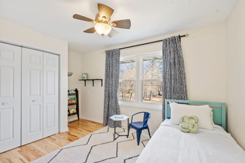 A well-decorated bedroom featuring a bed, blue chair, and books on a shelf.