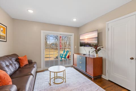 A cozy living room with a brown leather sofa, a coffee table, a wooden cabinet, and sliding glass doors opening to a yard.