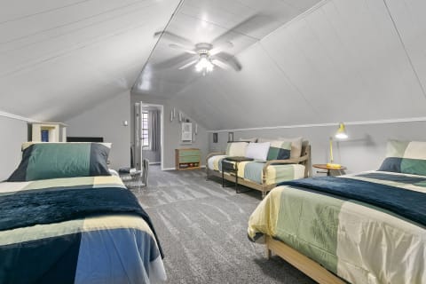 Attic bedroom featuring three beds with patchwork quilts and warm decor.