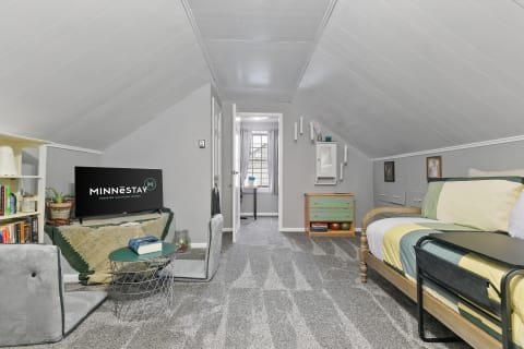 A cozy attic room with a bed, seating area, and window.