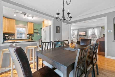 A dining area with a dark wooden table, bar stools, and an open view into a light-colored kitchen.