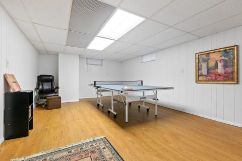 A well-lit basement room with a ping pong table, a reclining chair, and a decorative painting.