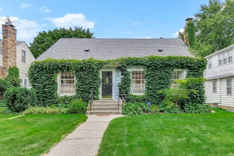 A bungalow covered with green ivy and surrounded by a well-kept lawn and shrubs.