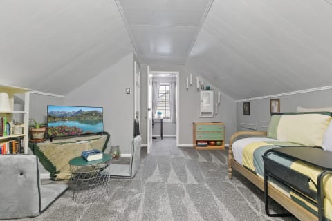 A welcoming attic room featuring a TV, a bed, and a workspace with natural light.
