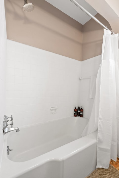 A bright bathroom with a white bathtub, beige wall, and shower curtain.
