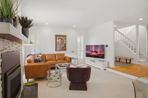 Contemporary living room with tan leather sofa, entertainment center, and staircase.