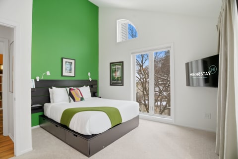 A modern bedroom featuring a green accent wall, white bedding, and large windows for natural light.