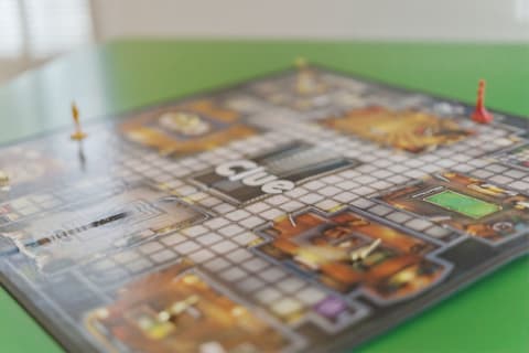 Close-up view of a Clue board game on a green table with game pieces visible.