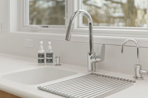 A modern kitchen sink with a chrome faucet and drying rack, illuminated by natural light from a window.