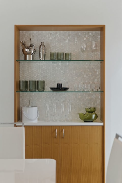 A chic bar display featuring shelves of cocktail essentials and various glassware against a textured backdrop.