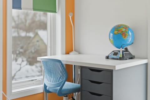 A modern study space featuring a white desk, a blue chair, and a globe with colorful geography.