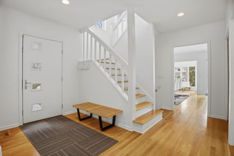 A bright and modern entryway with wooden bench and staircase.