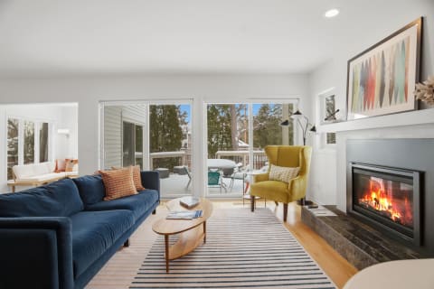 Cozy living room with navy sofa, yellow chair, fireplace, and view of a snowy balcony.