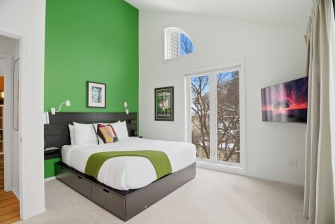 A modern bedroom featuring a green accent wall, white linens, and a cozy atmosphere.