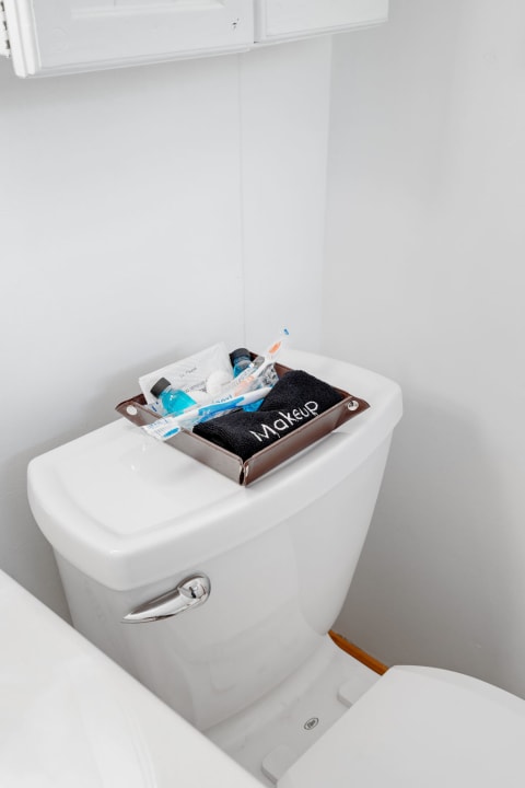 Toilet tank with a brown tray holding makeup items and a black towel labeled 'Makeup'.