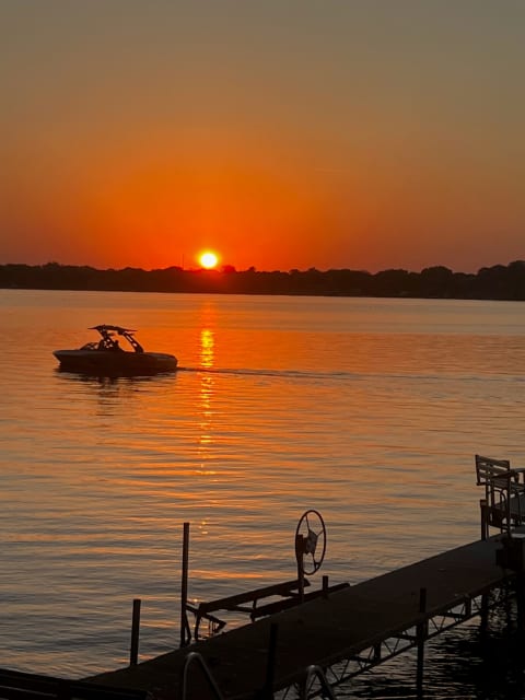 Sunset over a lake with a boat and a wooden dock in the foreground.
