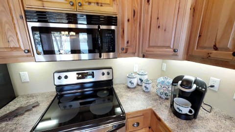 A cozy kitchen featuring wooden cabinets, a stove, microwave, coffee maker, and decorative canisters.