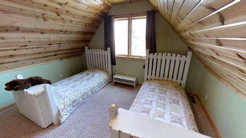 A cozy attic room featuring two twin beds with white picket fence headboards and a window with dark curtains.