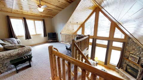 Spacious living room with wooden beams, large windows, and stone fireplace.
