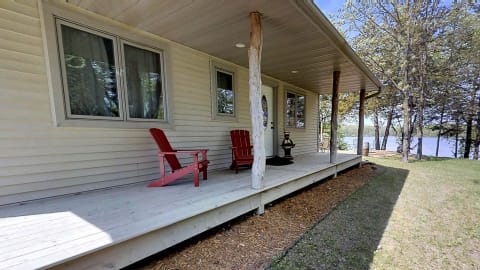 Lakeside home with red chairs on the porch and clear sky.