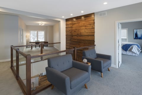 A stylish room with grey armchairs, wooden wall accents, and a view into another room.