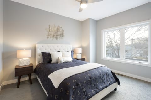 A modern bedroom featuring a white tufted headboard, navy blue bedding, and a large window.