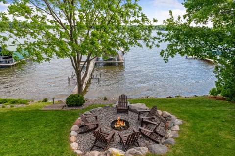 A lakeside fire pit area with Adirondack chairs and a dock in the background.