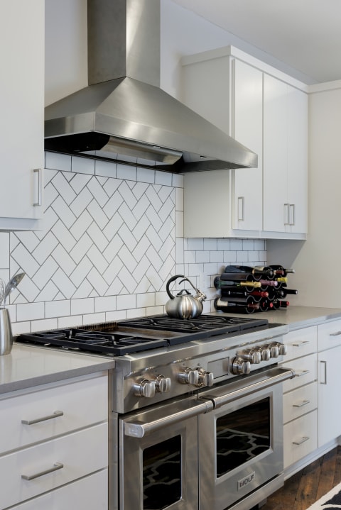Contemporary kitchen featuring a gas stove, ventilation hood, and white cabinets.