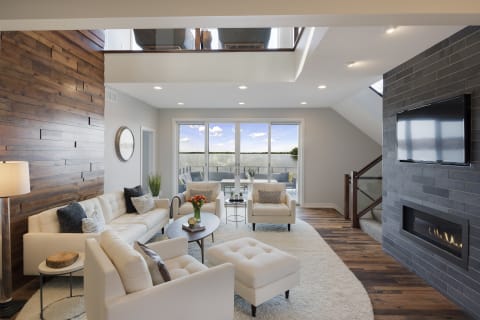 Modern living room with large windows overlooking water, featuring comfortable seating and warm decor elements.