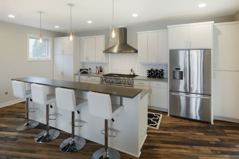 Modern kitchen featuring a long island with barstools, stainless steel appliances, and white cabinetry.