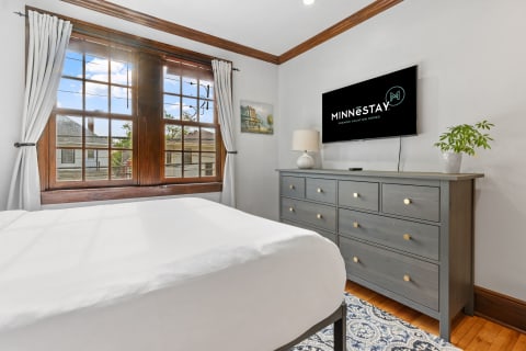 Cozy bedroom with a large window, gray dresser, and flat-screen TV.