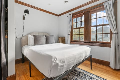 A cozy bedroom featuring a queen-sized bed, wooden windows, and a vintage radiator.