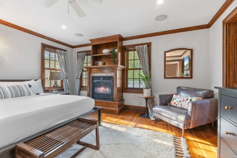 A cozy bedroom with a bed, a fireplace, and a leather armchair.