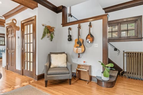 A comfortable corner featuring a gray armchair, musical instruments on the wall, and natural decor elements.
