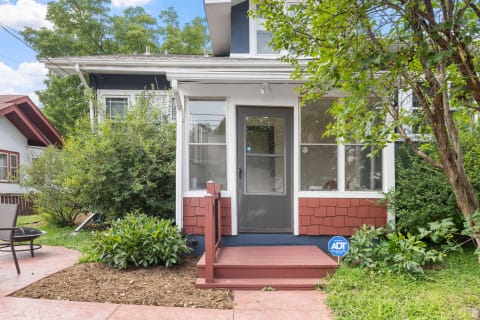 Front view of a two-story house featuring a porch and surrounded by greenery.