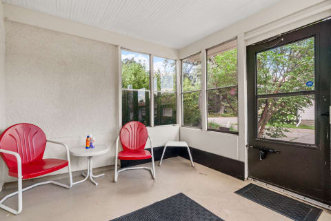 Screened porch with red chairs, a small table, and greenery visible outside.