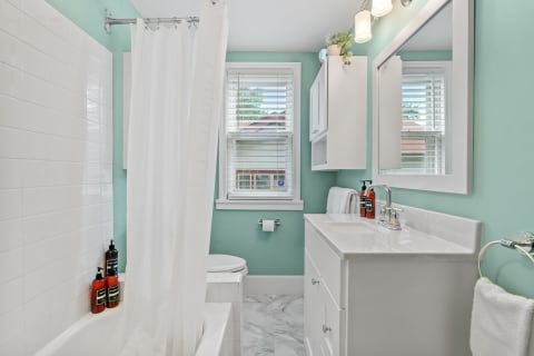 A modern bathroom featuring teal walls, a white shower curtain, and a marble floor.