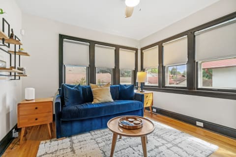 Cozy living room with blue sofa, wooden shelves, and large windows.