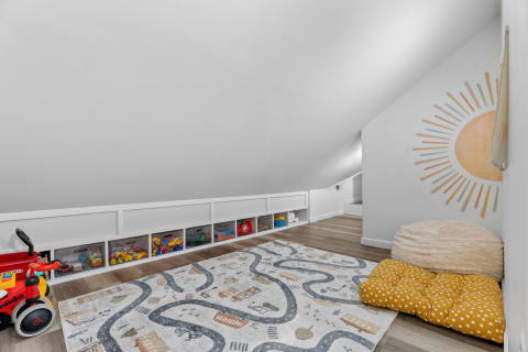A cozy attic playroom featuring a slanted ceiling, colorful bins, a playful rug, and comfortable seating.