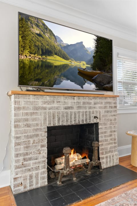 Living room with a TV displaying a mountain landscape over a rustic fireplace with a fire burning.