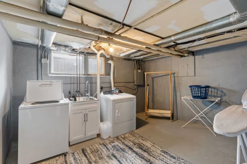 Basement laundry area with washing machine, sink, drying rack, and ironing board.