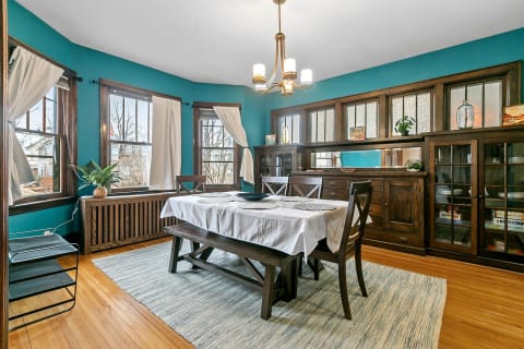 Dining room with turquoise walls and dark wooden furniture, featuring a large table and natural light from windows.